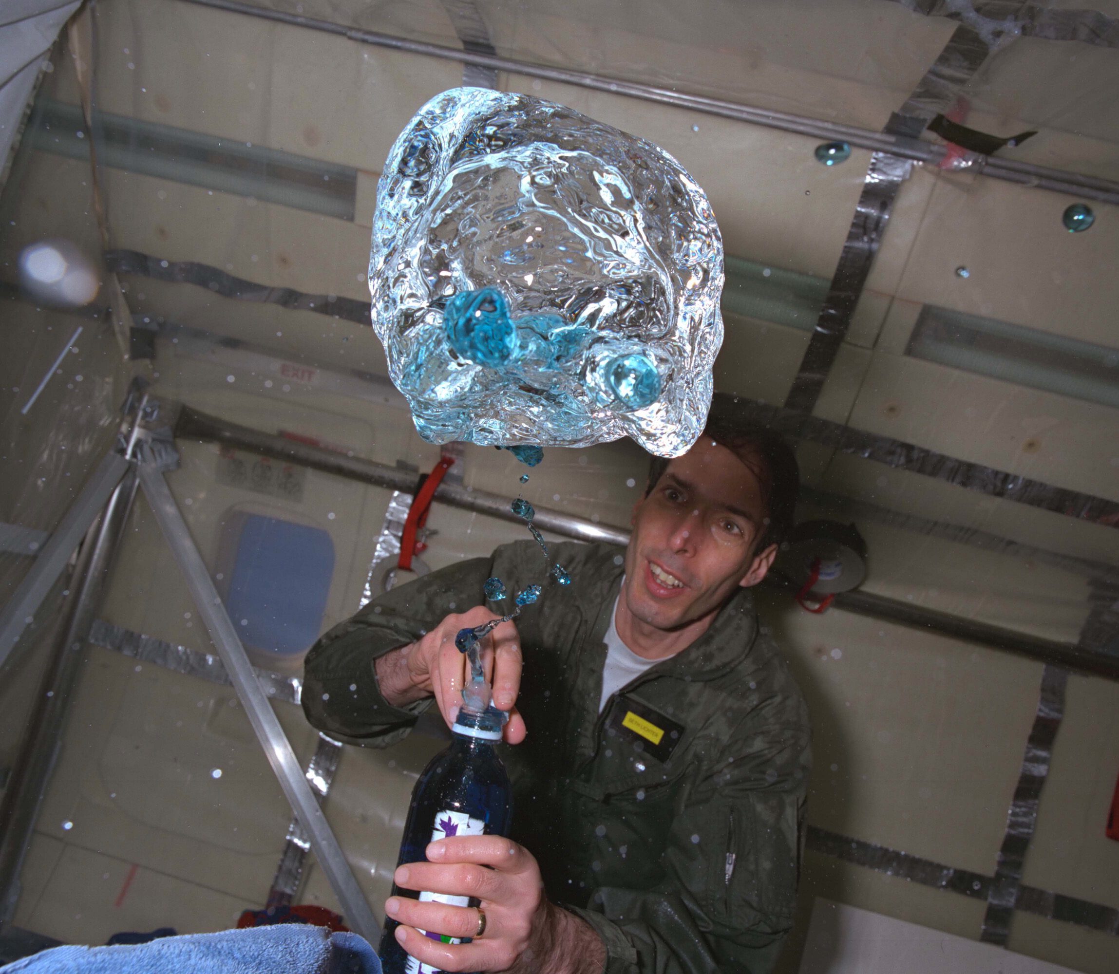 grc 1997 c 02184 e1732721530755.jpg A person in a green flight suit watches as blue fluid floats out of a bottle during a microgravity flight.
