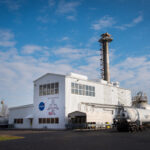 NASA Glenn Honored with Aviation Award for “NEAT” Success A metal building with an airplane and NASA logo on the front. A tall section is in the middle, a smaller flat section is on the left, and a large cylinder with tubing goes into the building on its right.