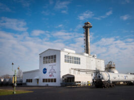 NASA Glenn Honored with Aviation Award for “NEAT” Success A metal building with an airplane and NASA logo on the front. A tall section is in the middle, a smaller flat section is on the left, and a large cylinder with tubing goes into the building on its right.