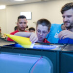 NASA Glenn’s Aviation Day Inspires Students to New Heights A researcher assists a student in guiding his cylindrical-shaped paper model into a tabletop demonstration unit.