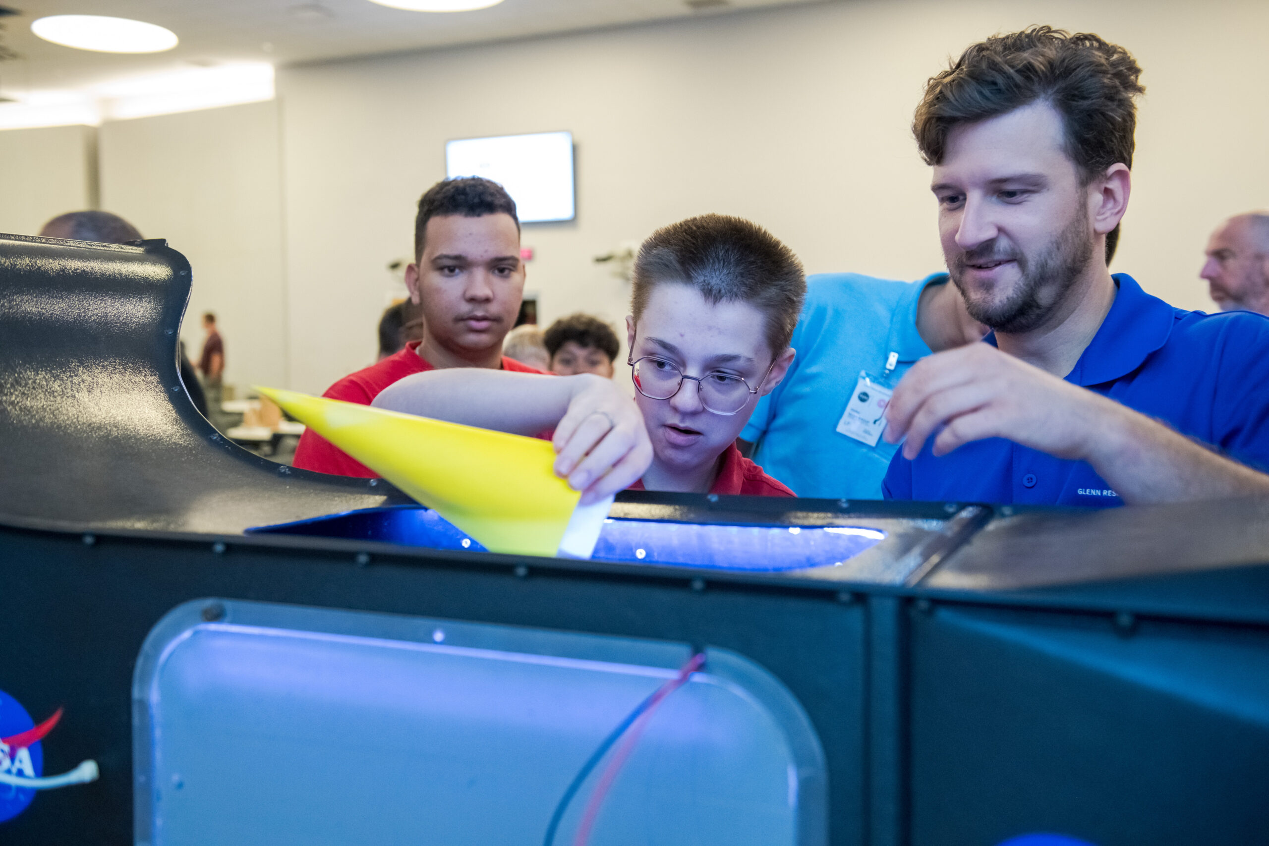 grc 2024 c 08875.jpg A researcher assists a student in guiding his cylindrical-shaped paper model into a tabletop demonstration unit.