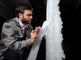 NASA Tests New Aircraft Wing for Critical Icing Conditions A man looks at white ice built up on a section of scale-model transonic truss-braced wing. The model wing stands vertically in NASA Glenn’s Icing Research Tunnel.