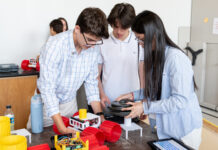 Apply for NASA Glenn’s Free Summer Engineering Institute now! Three High School Engineering Institute students are centered in the foreground of the image working on a small vehicle with large red plastic wheels. There are two more students in the background working on their own identical vehicle.