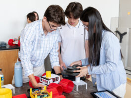 Apply for NASA Glenn’s Free Summer Engineering Institute now! Three High School Engineering Institute students are centered in the foreground of the image working on a small vehicle with large red plastic wheels. There are two more students in the background working on their own identical vehicle.