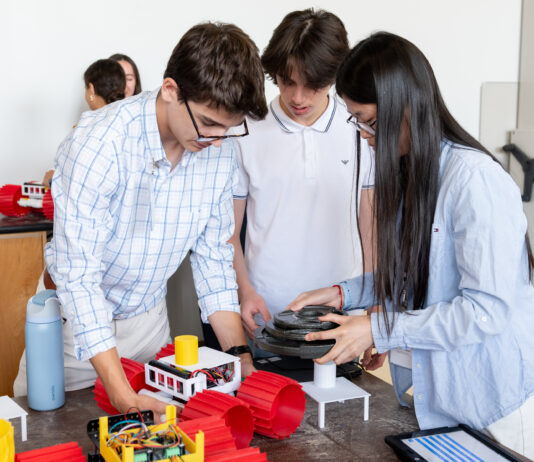 Apply for NASA Glenn’s Free Summer Engineering Institute now! Three High School Engineering Institute students are centered in the foreground of the image working on a small vehicle with large red plastic wheels. There are two more students in the background working on their own identical vehicle.