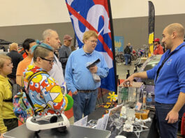 NASA Glenn Unveils Stirling Engine at Auto-Rama Event A NASA subject matter expert stands behind a display table and explains the technology behind free-standing piston Stirling engines to a group of people.