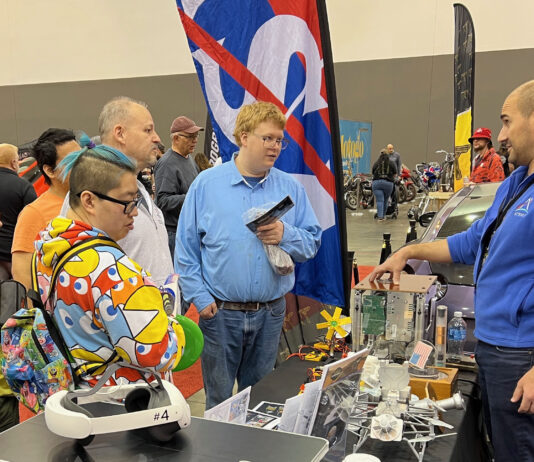 NASA Glenn Unveils Stirling Engine at Auto-Rama Event A NASA subject matter expert stands behind a display table and explains the technology behind free-standing piston Stirling engines to a group of people.