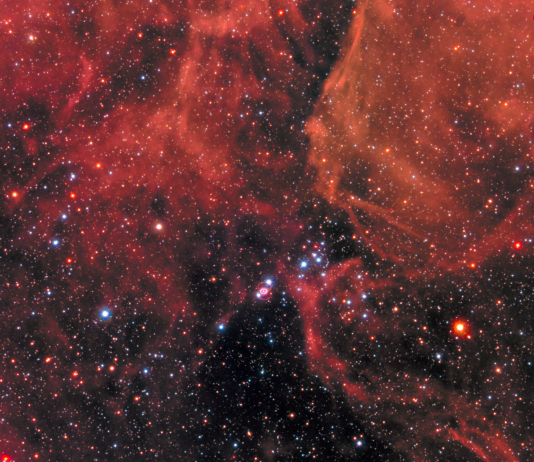 NASA Reveals Stunning Supernova Event Clouds of gas and dust in shades of red cover the top of the image and a little bit of the bottom. Right in the middle is Supernova 1987a, the remnant of an exploded star. The site of the supernova is surrounded by an illuminated pinkish ring. Two faint outer rings are also visible. Stars and galaxies shine throughout, giving off red and blue light.