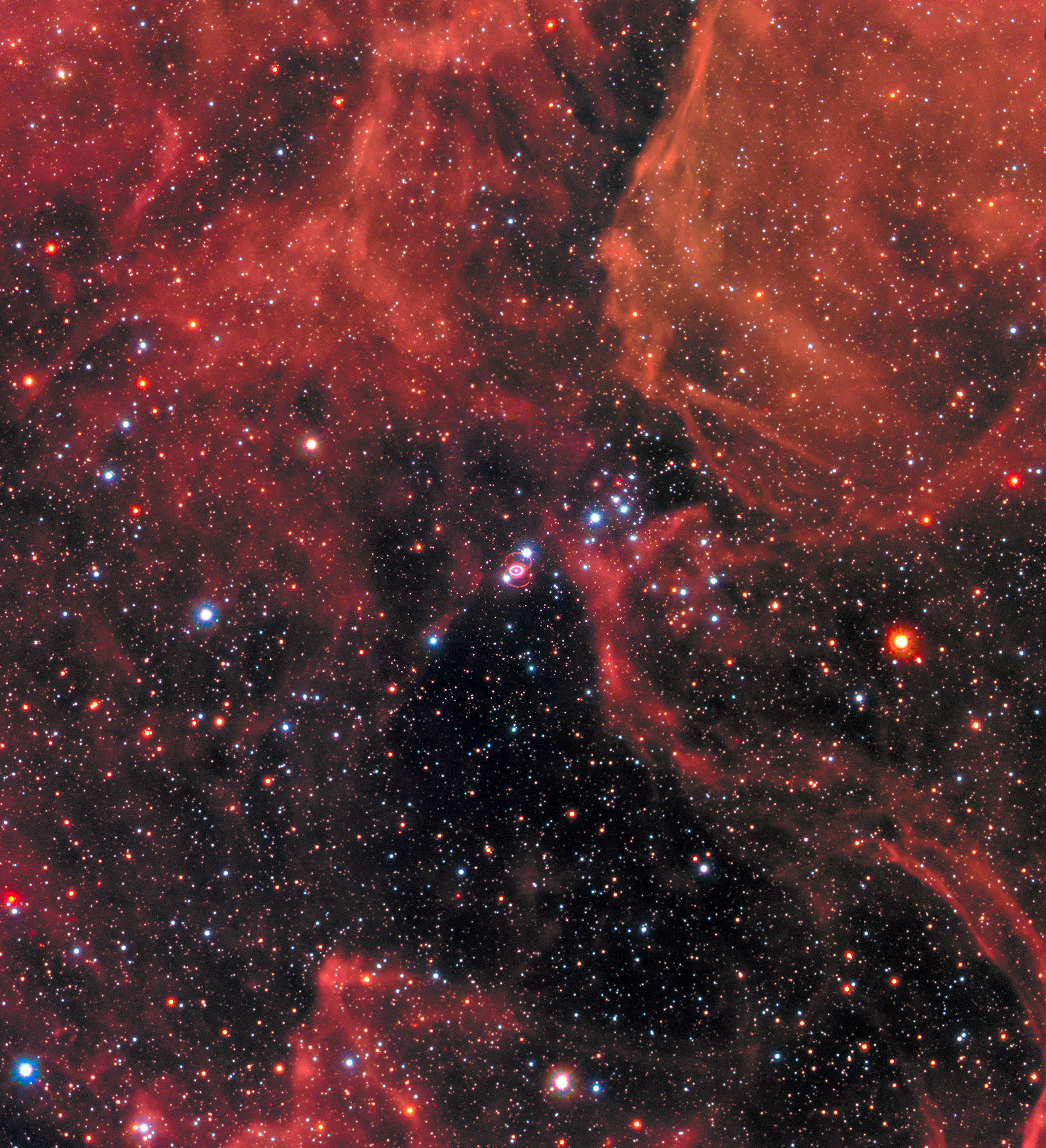 gsfc 20171208 archive e000102orig.png Clouds of gas and dust in shades of red cover the top of the image and a little bit of the bottom. Right in the middle is Supernova 1987a, the remnant of an exploded star. The site of the supernova is surrounded by an illuminated pinkish ring. Two faint outer rings are also visible. Stars and galaxies shine throughout, giving off red and blue light.