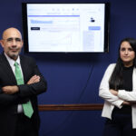 Puerto Rican company innovates AI solutions for business success. A man and a woman stand in front of a blue wall with a computer monitor between them