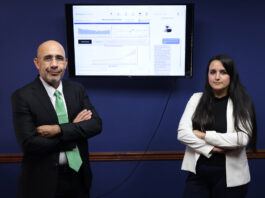 Puerto Rican company innovates AI solutions for business success. A man and a woman stand in front of a blue wall with a computer monitor between them