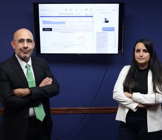 Puerto Rican company innovates AI solutions for business success. A man and a woman stand in front of a blue wall with a computer monitor between them