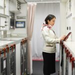 Japan Airlines adopts AI app for cabin crew reports A woman in a flight attendant’s uniform taps on a tablet in an airplane galley.