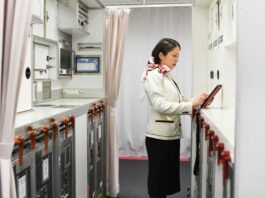 Japan Airlines adopts AI app for cabin crew reports A woman in a flight attendant’s uniform taps on a tablet in an airplane galley.