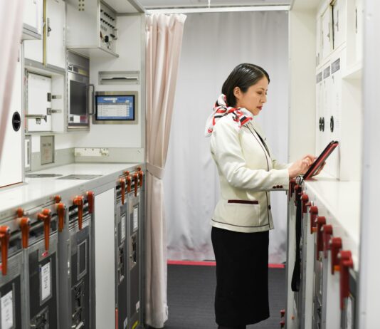 Japan Airlines adopts AI app for cabin crew reports A woman in a flight attendant’s uniform taps on a tablet in an airplane galley.