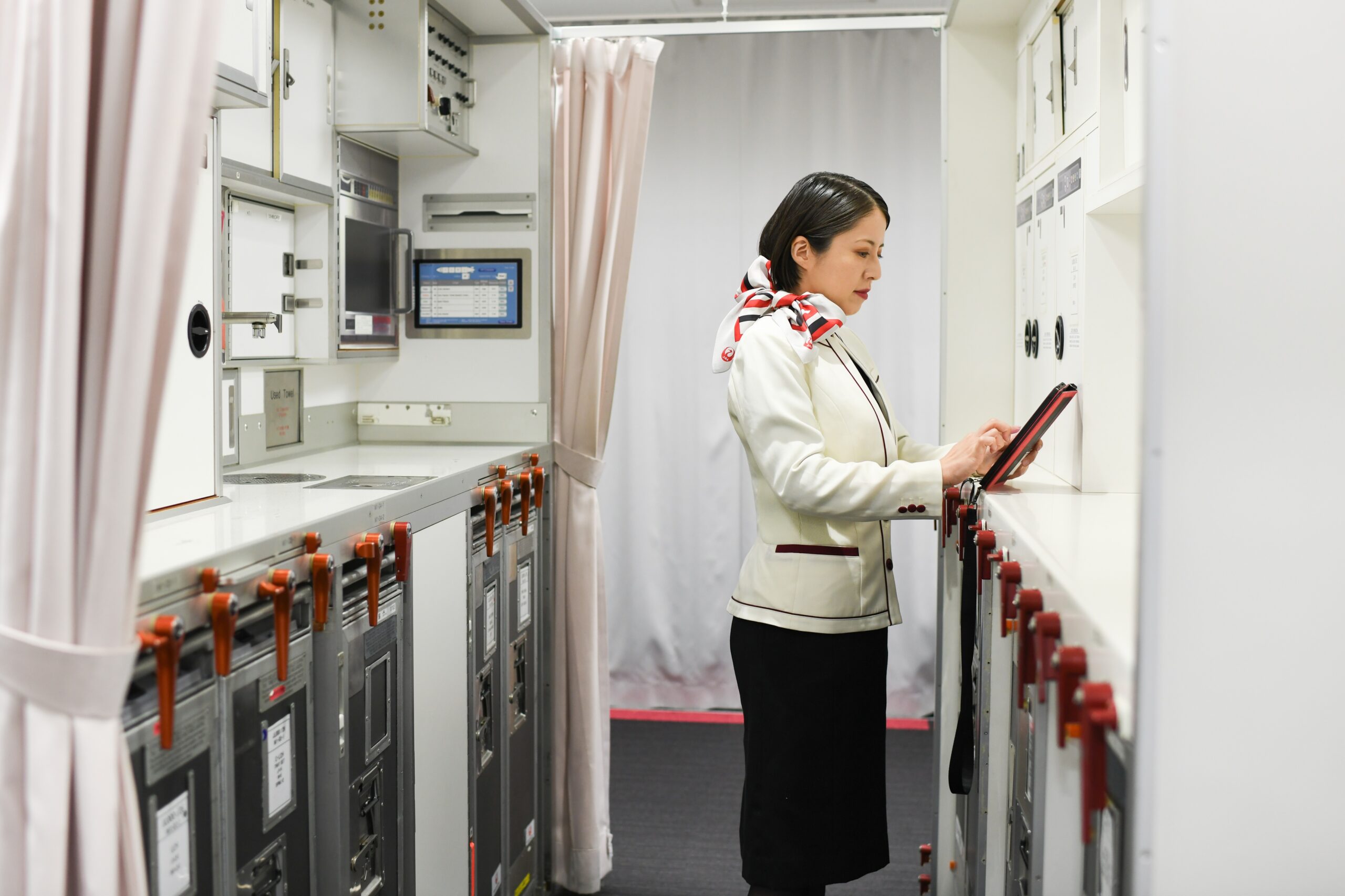 hero 4 scaled.jpg A woman in a flight attendant’s uniform taps on a tablet in an airplane galley.