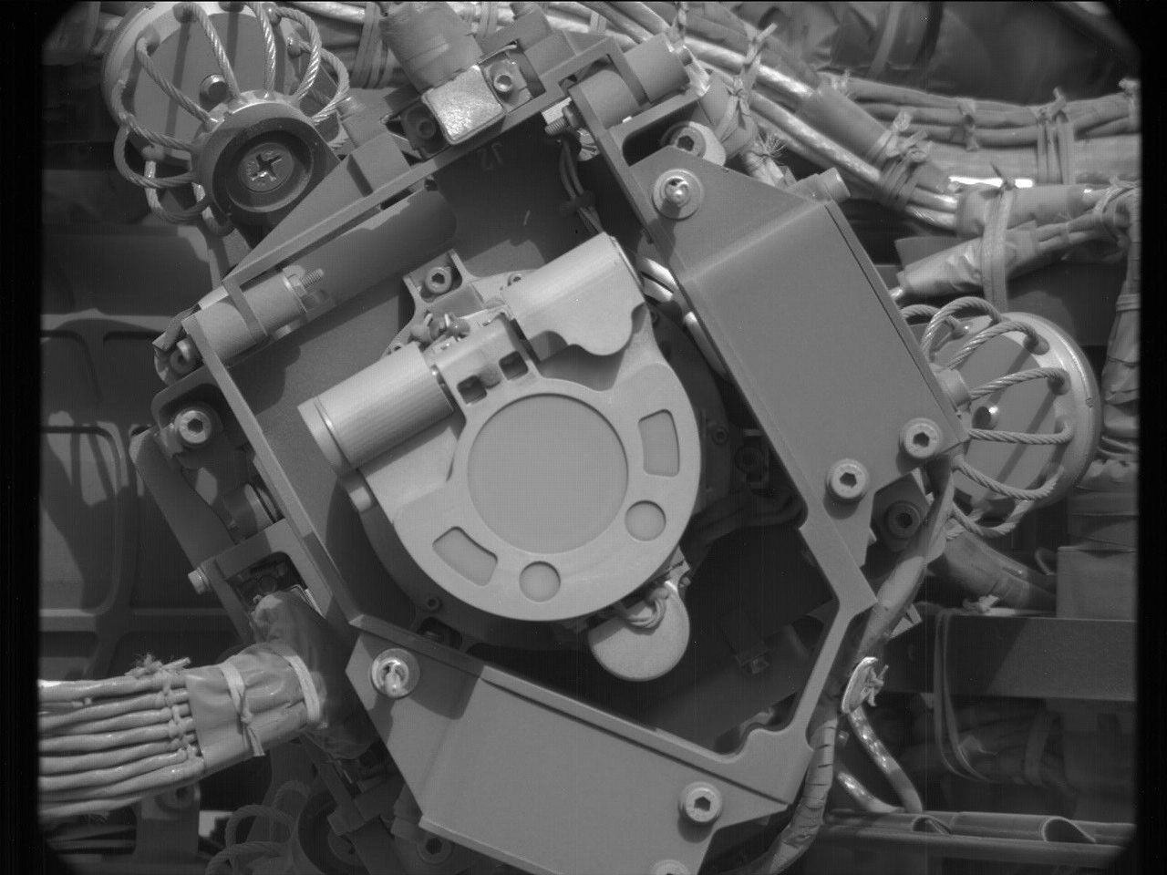 https mars.nasa .gov msl raw images msss 04291 mcam 4291mr1063250002200228c00 dxxx.jpg A grayscale close-up image of an instrument on the Mars rover Curiosity, showing at the center of the image a U-shaped flat piece of metal face the camera, with its rounded bottom pointing toward the lower right corner of the image. It’s surrounded by metal plates at different angles, some parallel to the plane of the image, others perpendicular, and most of them secured with hex nuts. Braided bunches of cable are twisted behind these other sections, leading into the instrument.