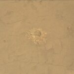 Examining Altadena Drill Site: NASA’s Curiosity Insights A color close-up photo of the Martian surface shows flat, mostly smooth, tan-orange ground, crisscrossed with a few shallow grooves and indentations. At the center is a hole cored into the ground, surrounded by a pile of soil and small rocks dug from the hole — those are similarly colored to the surrounding ground, but in shades ranging from lighter and more yellow to darker and deeper orange. Some of the back wall of the interior of the hole is also visible.