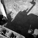 NASA Seeks Boxwork Bedrock Drill Site on Sols 4559-4560 A grayscale photo looking down at the Martian surface, showing very rough terrain in front of the Curiosity rover. Light gray, gravel-covered rocks are in bright sunlight in the upper half of the frame. A shadow silhouette of the rover covers much of the rest of the image, from the center toward the lower right corner. Portions of the rover itself are sunlit and visible at the bottom and left side of the image.