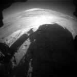 NASA Science: Curiosity Blog Explores Ridge on Sols 4616-4617 An extreme wide-angle, grayscale photo from the Mars surface shows uneven terrain ahead of the rover, covered in numerous small to medium-sized rocks, all light gray and illuminated by sunlight. Impressions in the middle ground ahead form swooping backward Cs, and in the far distance a mountain rises from the ground, but looks very broad and squat, because of the distortion from the wide-angle lens. Parts of the rover are visible around the sides and bottom of the image, and its shadow fills much of the foreground.