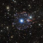 Telescopes collaborate to capture Cat’s Eye Nebula from new angles A planetary nebula in space. The star in the very center is surrounded by white bubbles and loops of gas, all shining with a powerful blue light. Farther away a broken ring of red and blue gas clouds surrounds the nebula. A multitude of golden and white stars, wisps of gas and distant galaxies of various sizes surround the nebula on the black background.