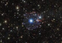 Telescopes collaborate to capture Cat’s Eye Nebula from new angles A planetary nebula in space. The star in the very center is surrounded by white bubbles and loops of gas, all shining with a powerful blue light. Farther away a broken ring of red and blue gas clouds surrounds the nebula. A multitude of golden and white stars, wisps of gas and distant galaxies of various sizes surround the nebula on the black background.