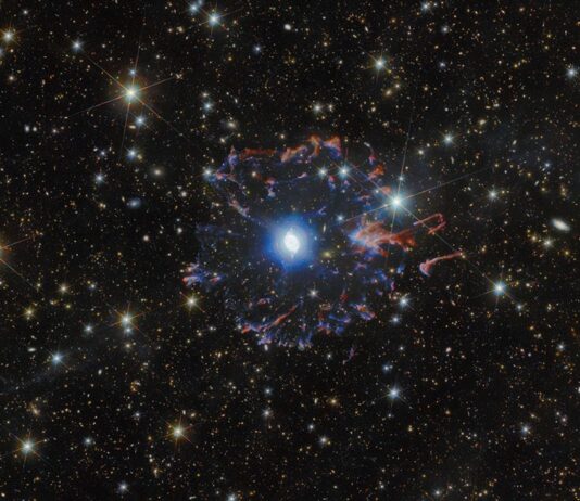 Telescopes collaborate to capture Cat’s Eye Nebula from new angles A planetary nebula in space. The star in the very center is surrounded by white bubbles and loops of gas, all shining with a powerful blue light. Farther away a broken ring of red and blue gas clouds surrounds the nebula. A multitude of golden and white stars, wisps of gas and distant galaxies of various sizes surround the nebula on the black background.