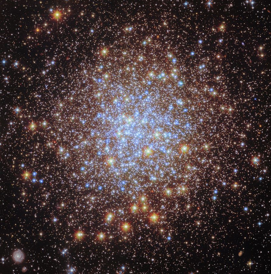 hubble m72 potw2516a.jpg Thousands of bright stars fill a spherically shaped globular cluster. In the center, most of the stars appear blue. The globular cluster’s bright blue-white core is surrounded by a thick shell of yellower stars, seen in differing sizes according to their position in the spherical star cluster. They spread out beyond the edges of the image, appearing smaller and sparser at the corners of the image. A distant spiral galaxy is also visible in the lower-left corner of the image.
