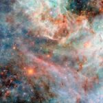 NASA’s Hubble Snaps Images of Cotton Candy-Like Clouds Part of a nebula in space. Layers of gas and dust clouds in different colors, from blue and green shades to pink, red, and black, each indicating light emitted by different molecules, comprise the nebula. The background cloud layers are thicker and puffier, though still translucent, and the upper layers are thin and bright at the edges. Behind the clouds are many small, mostly orange and some blue, stars.