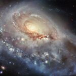 NASA’s Hubble Captures Unusual Spiral Galaxy Image A spiral galaxy seen at a skewed angle. Its center is a bright spot radiating light. A thick, stormy disk of material surrounds this bright center, with swirling strands of dark dust and bright spots of star formation strewn through the disk. A large spiral arm extends from the disk toward the viewer. Some foreground stars are visible atop the galaxy.