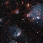 Hubble, Webb Telescopes Uncover Dual Views of Star Cluster Bluish clouds of gas are wound through with red-glowing lanes and filaments of dust.. The clouds contain cavities filled with stars and many more stars are visible in the background and scattered throughout the clouds. The clouds are concentrated in the upper right and the lower middle of the image. Tiny background galaxies are also sprinkled throughout the image.