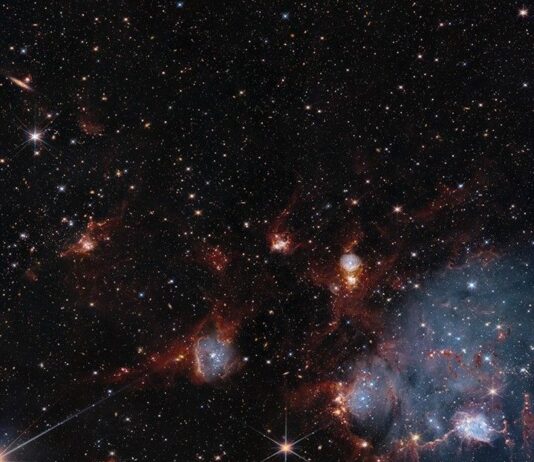 Hubble, Webb Telescopes Uncover Dual Views of Star Cluster Bluish clouds of gas are wound through with red-glowing lanes and filaments of dust.. The clouds contain cavities filled with stars and many more stars are visible in the background and scattered throughout the clouds. The clouds are concentrated in the upper right and the lower middle of the image. Tiny background galaxies are also sprinkled throughout the image.