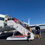 Retired DC-8 Aircraft Inspires Students Beyond Textbooks – NASA A group of 22 students pose on a stairway descending from an aircraft door. The plane and stairway are white, on a sunny tarmac.