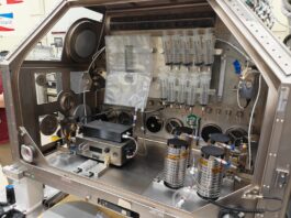 NASA Develops Technology to Produce IV Fluids in Space A large metal housing box containing the IVGEN Mini system is set up to create IV fluid. It includes the filtering system (two small boxes with cords attached), one plastic input bag, one plastic output bag, 10 syringes, additional cording, and four silver cylinder-shaped pieces of equipment.