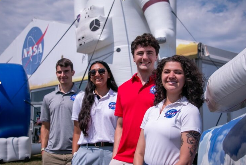 Four NASA interns pose in front of the NASA Pavilion at the EAA AirVenture Oshkosh, an annual airshow in Oshkosh, Wisconsin