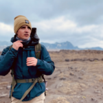 NASA’s Dr. Michael Thorpe: Expert in Sedimentary and Planetary Geology A man wearing a tan beanie and a blue winter jacket with a hiking backpack strapped around him. He