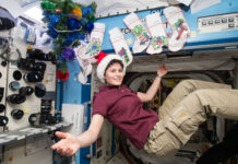 NASA: Festive Season Celebrations in Space A woman with short, dark hair and wearing a Santa hat, maroon shirt, and khaki pants smiles with arms outspread while floating in microgravity in front of Christmas stockings.