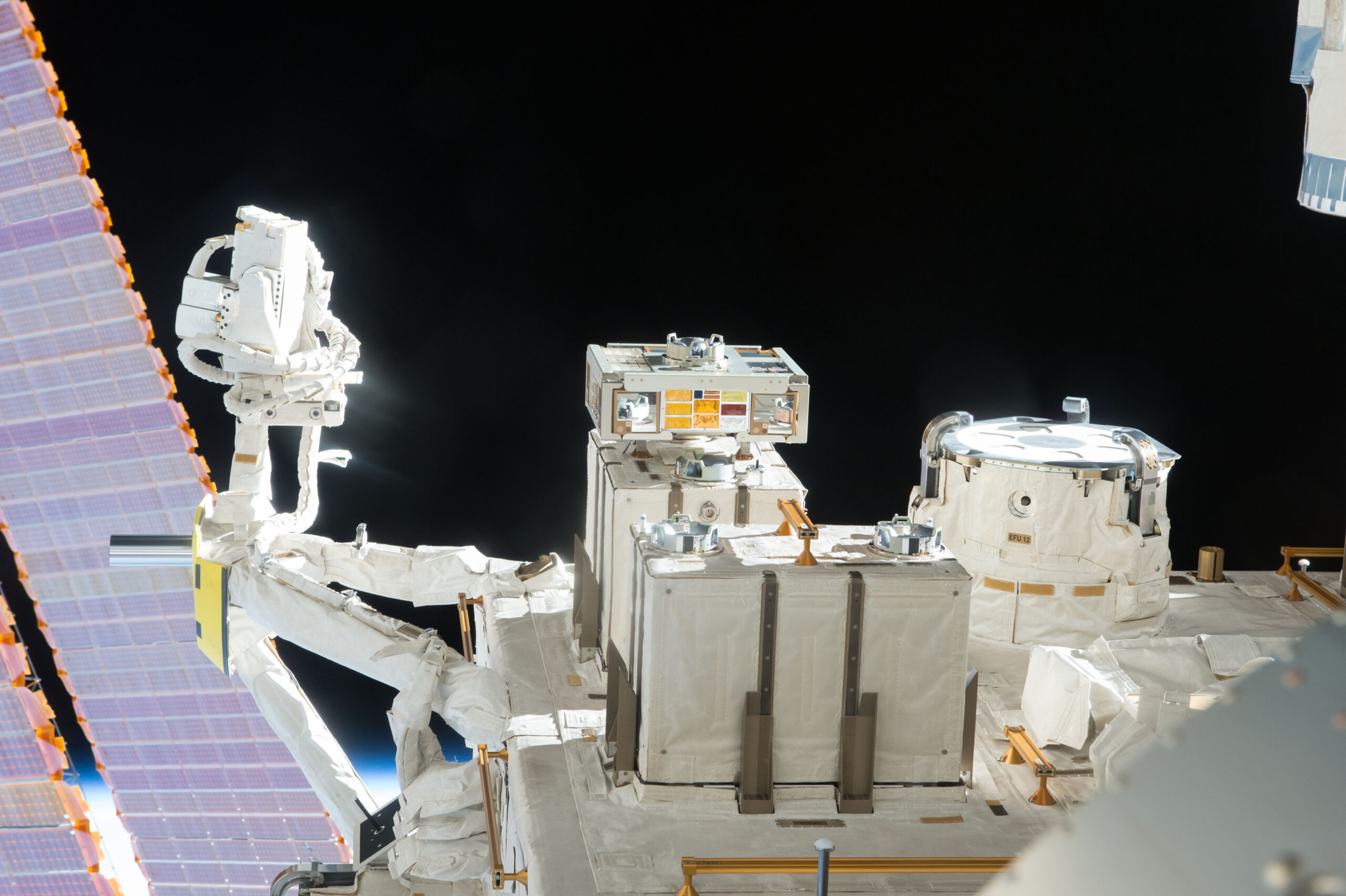 iss048e025920.jpg A view of an exposed module outside the International Space Station with solar panels and the darkness of space behind it.