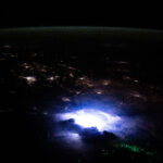 NASA Explores Lightning Phenomena in Southeast Asia Southeast Asia occupies the bottom two-thirds of the image. The scene is dark except for nighttime lights coming from urban areas, the white and purple glow from a thunderstorm, and green dots from fishing boats. A strip of green airglow is visible across the planet