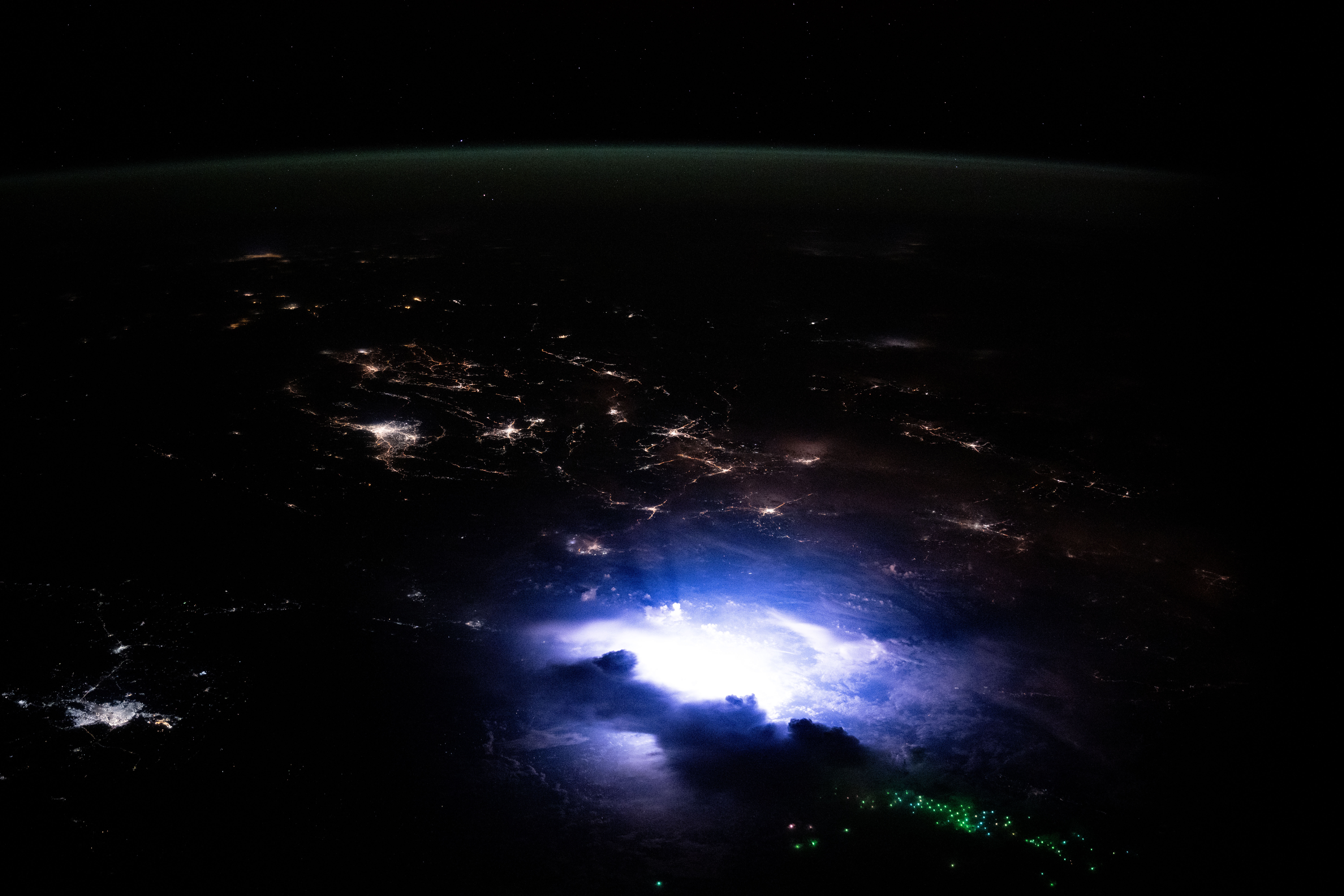 iss072e125247.jpg Southeast Asia occupies the bottom two-thirds of the image. The scene is dark except for nighttime lights coming from urban areas, the white and purple glow from a thunderstorm, and green dots from fishing boats. A strip of green airglow is visible across the planet