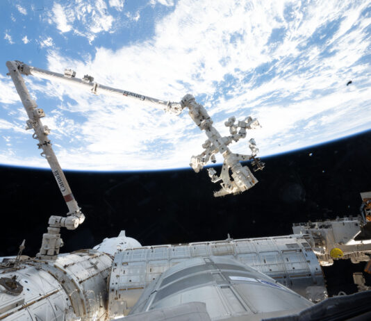 NASA Leverages Robotics for Assistance The 57.7-foot-long Canadarm2 robotic arm extends from the International Space Station. The arm is long, cylindrical, and white, with several joints that are bent to the right (at left in the image) and downward (at center). Earth makes a bright white and blue background for the top half of the photo. Our home planet contrasts starkly with the darkness of space.