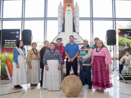 Kenneth Attocknie Connects Cultures at NASA Beyond Gaming A group of Indigenous people and a NASA employee pose together in front of a model of the Space Shuttle Endeavour. The individuals wear traditional clothing, including sashes and beaded garments.