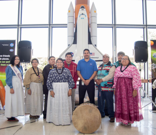 Kenneth Attocknie Connects Cultures at NASA Beyond Gaming A group of Indigenous people and a NASA employee pose together in front of a model of the Space Shuttle Endeavour. The individuals wear traditional clothing, including sashes and beaded garments.