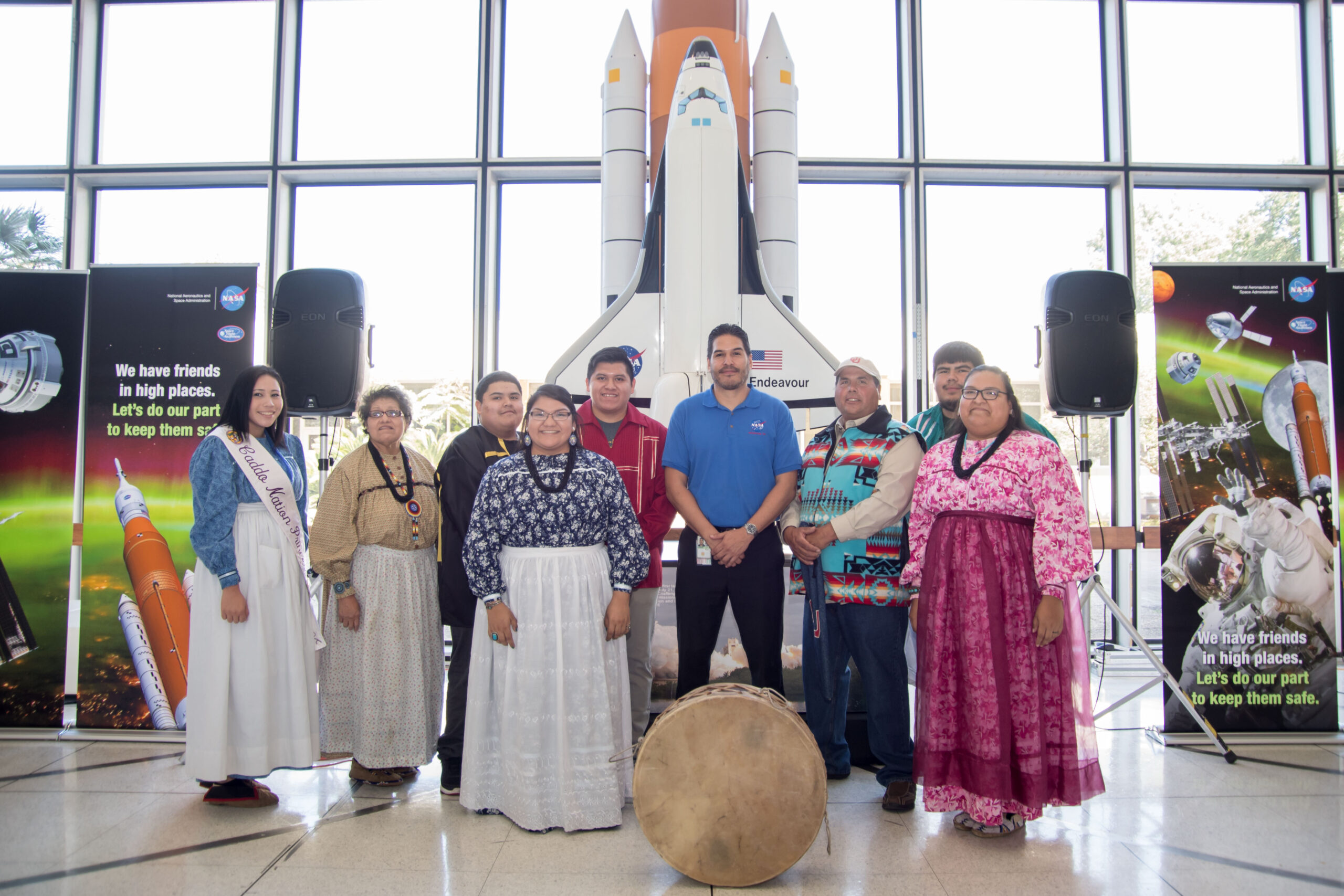 jsc2017e133259.jpg A group of Indigenous people and a NASA employee pose together in front of a model of the Space Shuttle Endeavour. The individuals wear traditional clothing, including sashes and beaded garments.