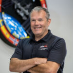 David Korth Appointed Deputy for NASA’s Safety Directorate A white, smiling male in a blue polo stands with arms folded in front of the International Space Station logo.