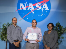 Jason Phillips’ Surprising Journey to NASA’s Johnson Procurement Jason Phillips stands between two managers on a stage with the NASA meatball in the background, holding an award.