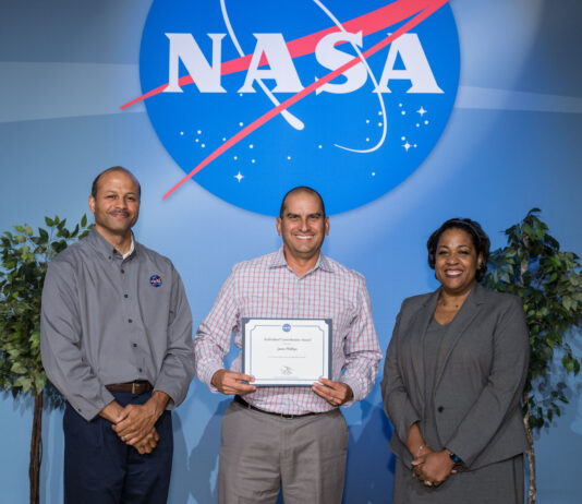 Jason Phillips’ Surprising Journey to NASA’s Johnson Procurement Jason Phillips stands between two managers on a stage with the NASA meatball in the background, holding an award.