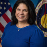 Jennifer Becerra: Pioneering STEM Influence at NASA Johnson A professional portrait of a woman with dark hair, wearing a blue top. She stands in front of the American flag and NASA’s emblem.