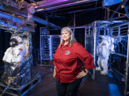 Caregivers at Johnson Balance Dual Roles with Community Support A woman stands inside a test chamber with several spacesuits.