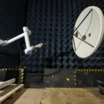NASA Enhances Lunar Communication with Electric Field Tests: Earth to Gateway In a testing facility, a robotic arm manipulates a probe to test the electric field of a large, white, circular dish antenna. This antenna is situated within an anechoic chamber, which is lined with dark blue, wedge-shaped foam.